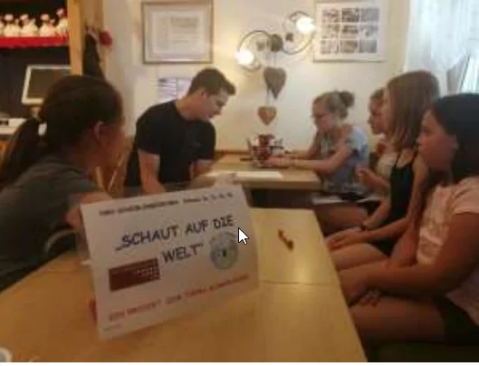 Schülerinnen und Schüler tauschen sich am Tisch zum Projekt Schaut auf die Welt aus.